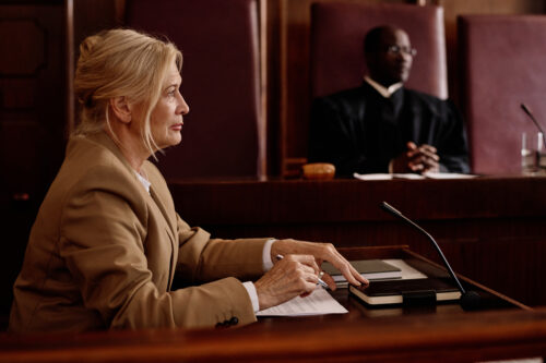 Side view of mature blond female witness or lawyer speaking in microphone while sitting against African American male judge