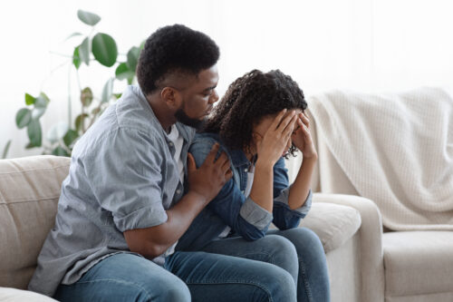 Dependent Relationship. Young Black Guy Soothing His Depressed Girlfriend At Home