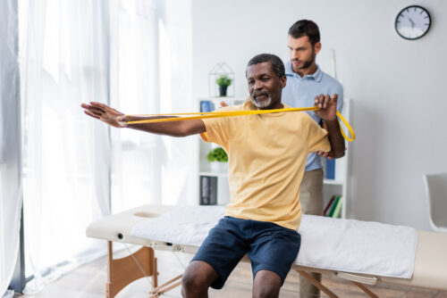 middle aged african american man sitting on massage table physical therapy