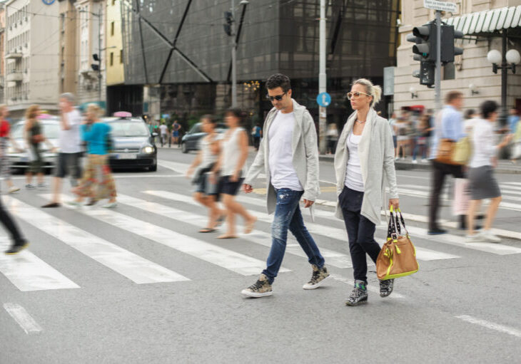 Happy fashionable couple crossing road at pedestrian zebra crossing in the city