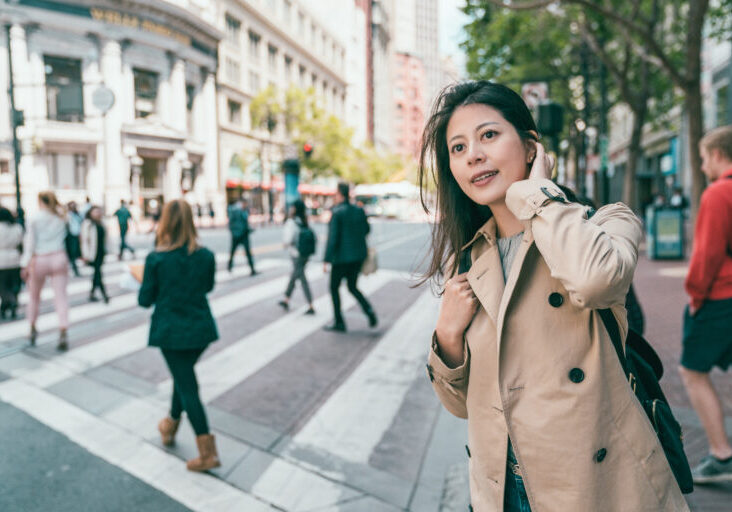 pretty woman looking around the city joyfully by the background of people crossing the road