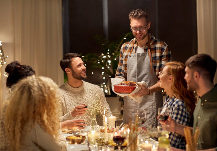 holidays, celebration and people concept - happy smiling friends having christmas dinner at home in evening