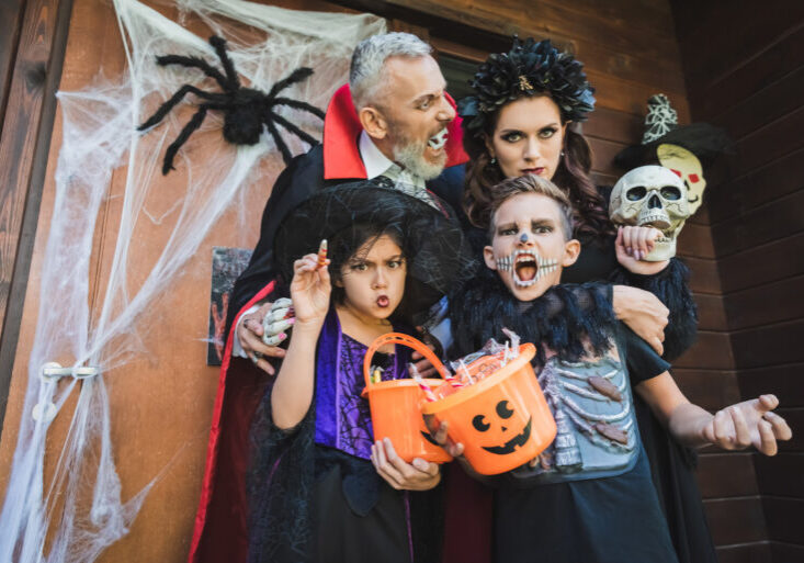 family in scary costumes grimacing near door with halloween decoration