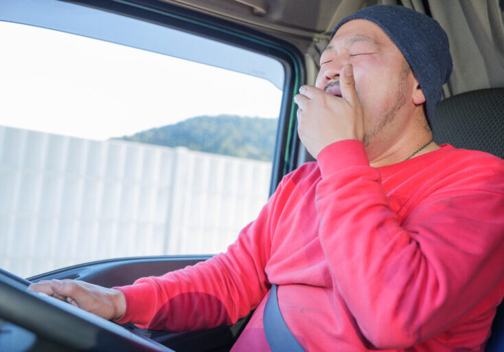 あくびをしながら大型トラックを運転している男性ドライバー